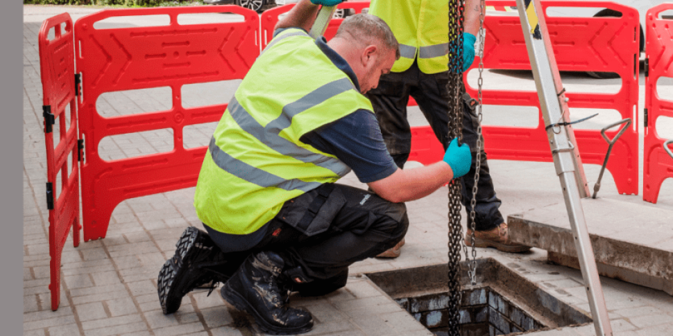 two engineers lowering a pump into a manhole
