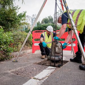 An image of two of our engineers lifting a sump pump of a sewer